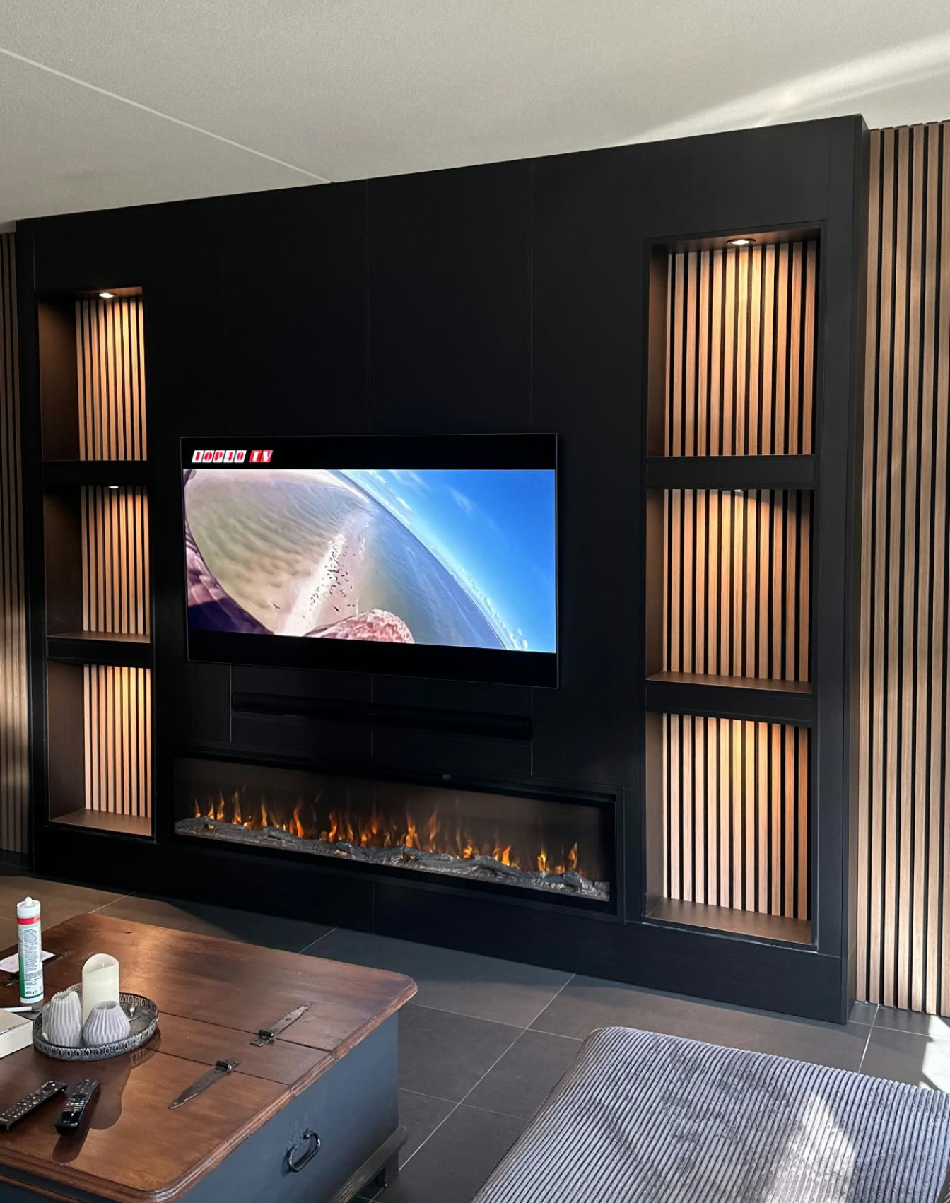 Door ons gerealiseerde zwarte cinewall met verlichte lattennissen, televisie en brede sfeerhaard