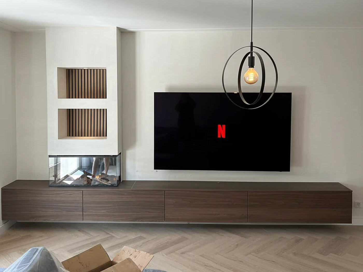 De cinewall in microcement met twee verlichte lattennissen, de driezijdige haard en een lang zwevend dressoir in notenhout